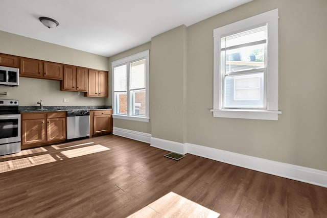 kitchen featuring baseboards, brown cabinetry, dark countertops, dark wood-style flooring, and stainless steel appliances