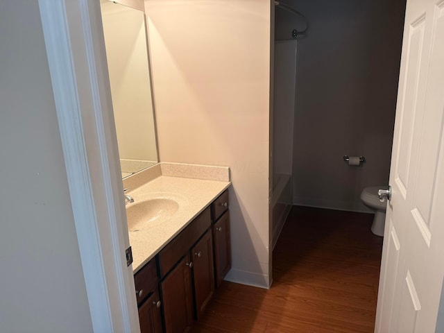 bathroom featuring toilet, wood finished floors, shower / bath combination, baseboards, and vanity