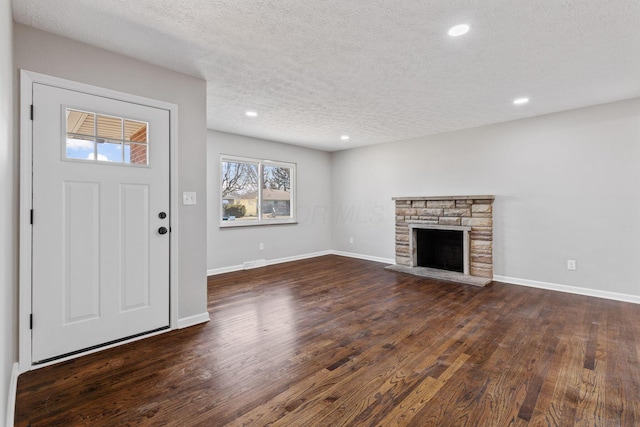 entryway with a textured ceiling, a stone fireplace, dark wood finished floors, and baseboards