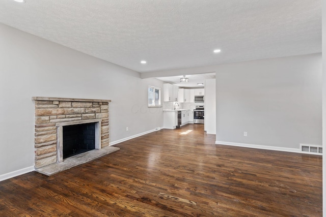 unfurnished living room featuring a sink, baseboards, dark wood-style flooring, and a stone fireplace