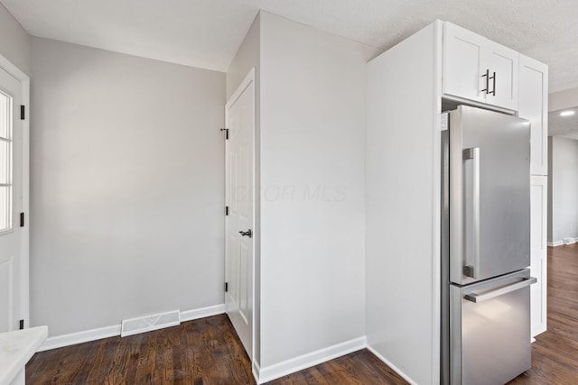 kitchen with visible vents, baseboards, dark wood-style floors, freestanding refrigerator, and white cabinetry