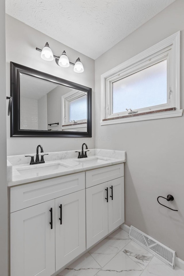 bathroom featuring marble finish floor, a textured ceiling, visible vents, and a sink