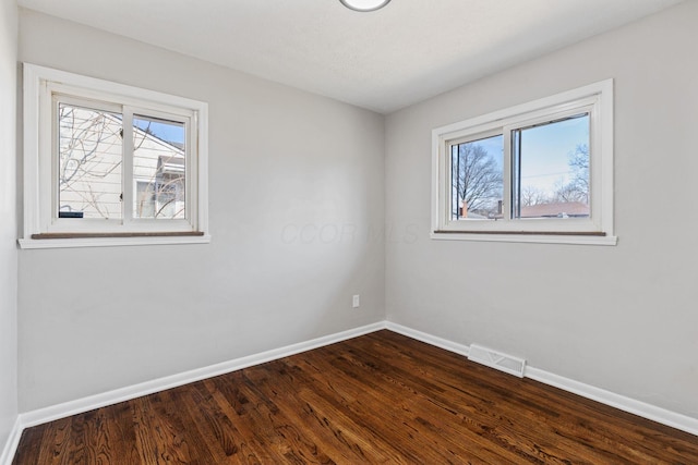 empty room with baseboards, wood finished floors, visible vents, and a healthy amount of sunlight