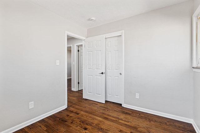 unfurnished bedroom featuring a closet, baseboards, and dark wood-type flooring