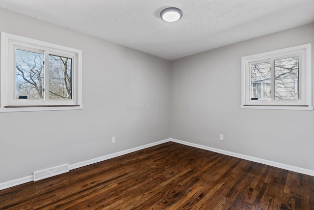 empty room featuring dark wood-style floors, baseboards, visible vents, and a textured ceiling