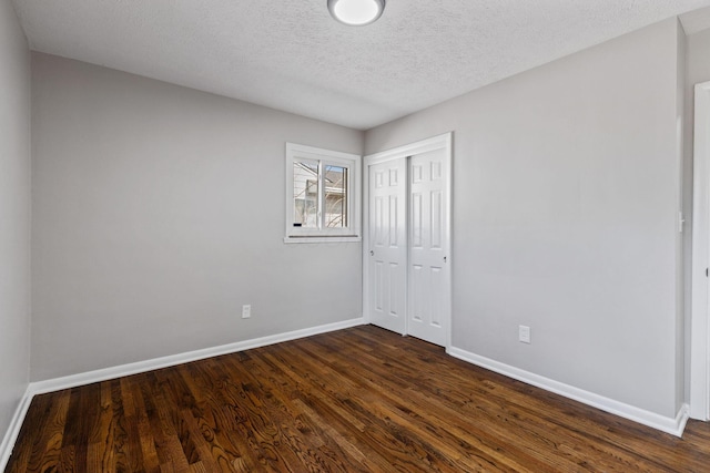 unfurnished bedroom featuring a textured ceiling, a closet, dark wood finished floors, and baseboards