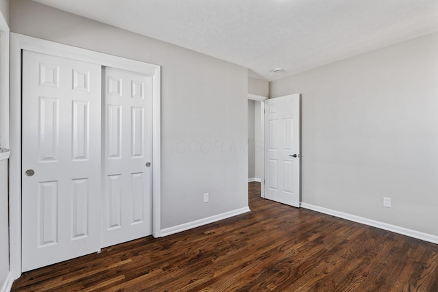 unfurnished bedroom featuring dark wood-style floors, a closet, a textured ceiling, and baseboards