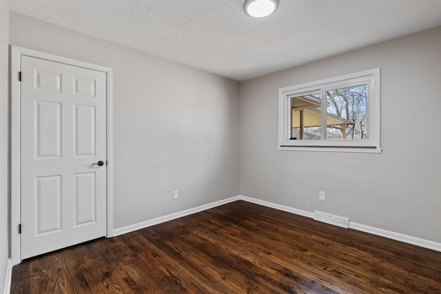 spare room featuring dark wood-style floors, visible vents, a textured ceiling, and baseboards