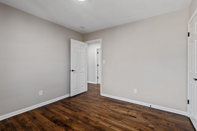 unfurnished bedroom with a textured ceiling, dark wood finished floors, and baseboards