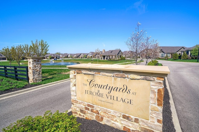 community sign with a lawn, a water view, fence, and a residential view