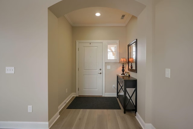 foyer entrance featuring arched walkways, crown molding, visible vents, wood finished floors, and baseboards