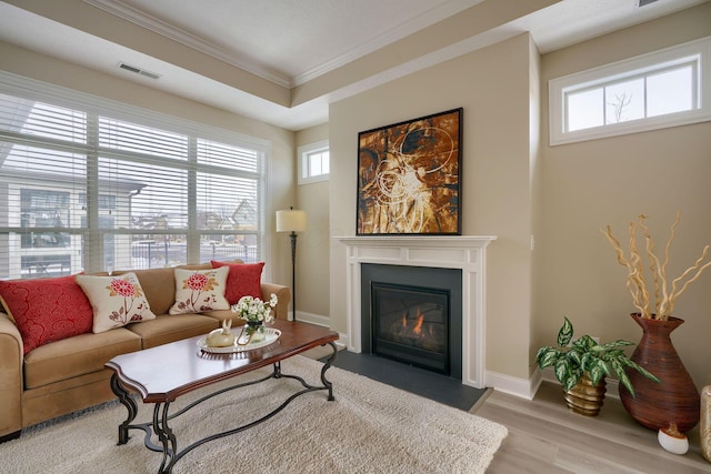 living area featuring ornamental molding, a wealth of natural light, a glass covered fireplace, and visible vents