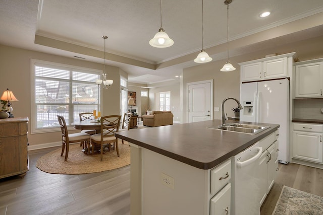 kitchen featuring white appliances, white cabinetry, dark countertops, a raised ceiling, and a center island with sink