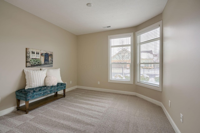 living area featuring baseboards, visible vents, and light colored carpet