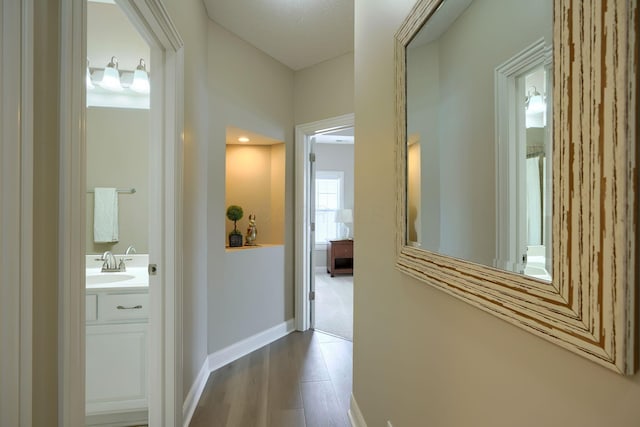 hallway with baseboards, a sink, and wood finished floors