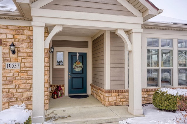 snow covered property entrance featuring stone siding and brick siding