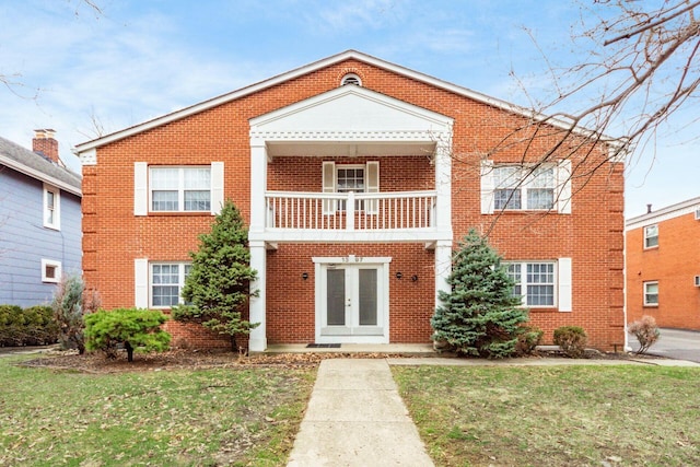 view of front of home with a front lawn, a balcony, french doors, and brick siding