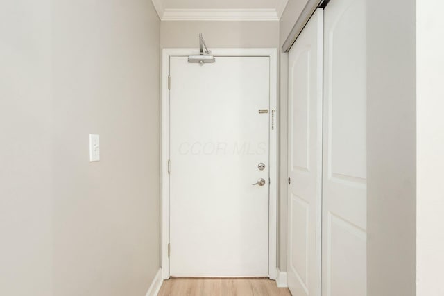 corridor featuring light wood-style flooring, crown molding, and baseboards