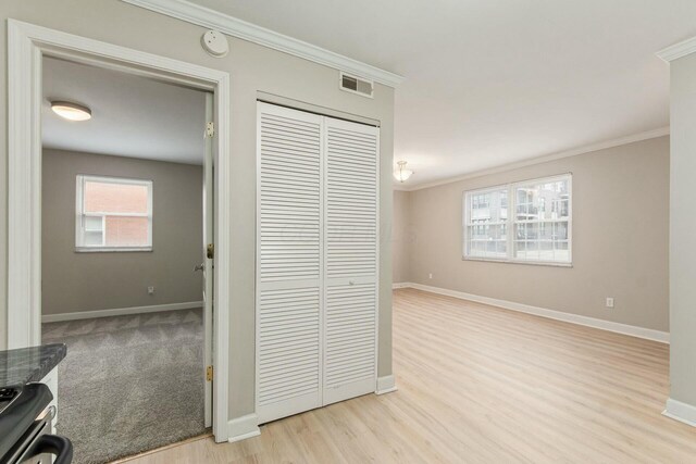 hall with light wood-style flooring, baseboards, visible vents, and ornamental molding