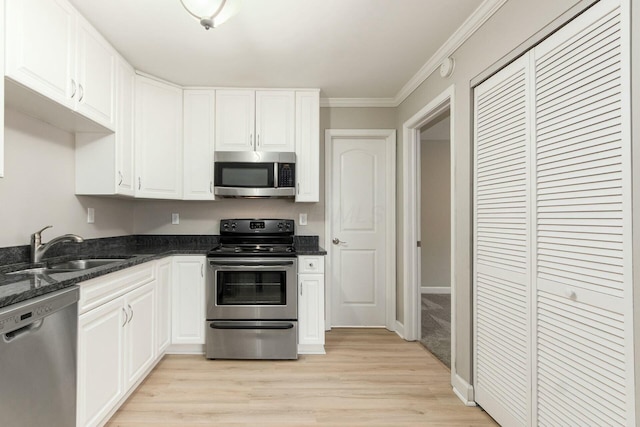 kitchen featuring ornamental molding, light wood-style floors, white cabinets, stainless steel appliances, and a sink