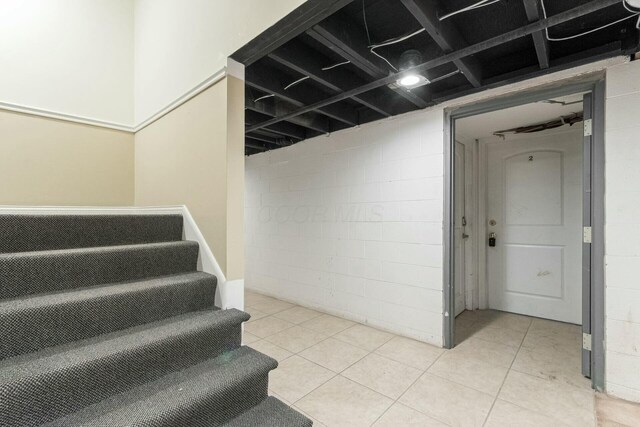 staircase with tile patterned floors and concrete block wall