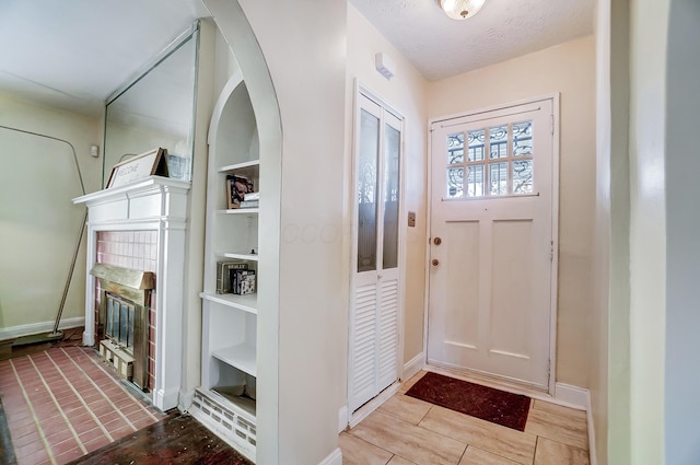 foyer featuring light wood finished floors, baseboards, arched walkways, a glass covered fireplace, and a textured ceiling