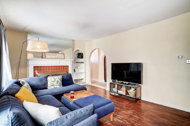 living room with arched walkways, a tiled fireplace, baseboards, and wood finished floors