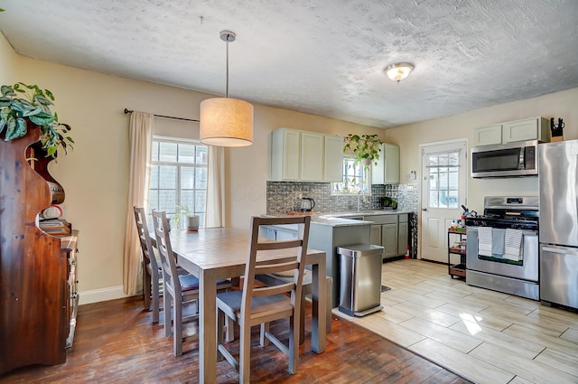 kitchen featuring light wood-style flooring, stainless steel appliances, light countertops, pendant lighting, and backsplash