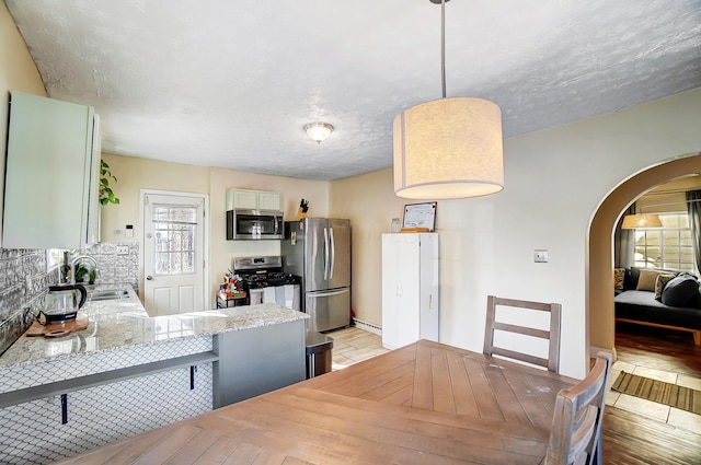 dining area featuring light wood-style flooring, arched walkways, and a textured ceiling