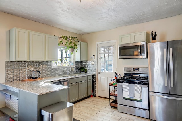 kitchen featuring a peninsula, a sink, appliances with stainless steel finishes, light stone countertops, and tasteful backsplash