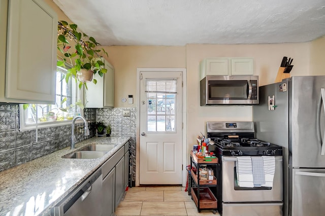 kitchen with a textured ceiling, light stone counters, a sink, appliances with stainless steel finishes, and backsplash