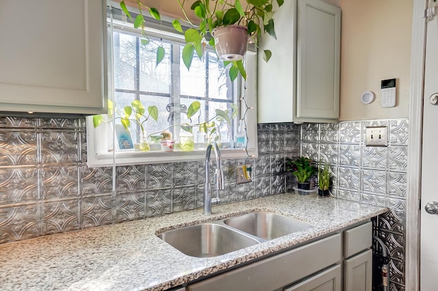 kitchen with light stone counters, gray cabinets, a sink, and decorative backsplash