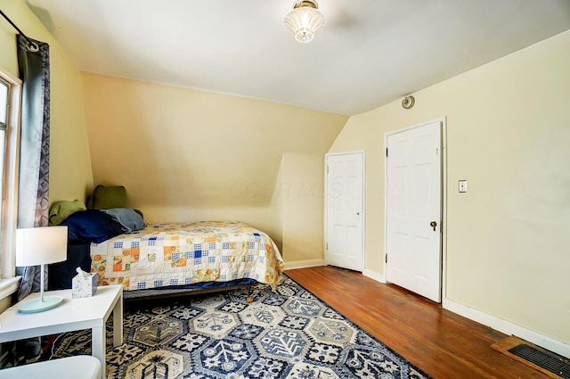 bedroom with lofted ceiling, wood finished floors, visible vents, and baseboards