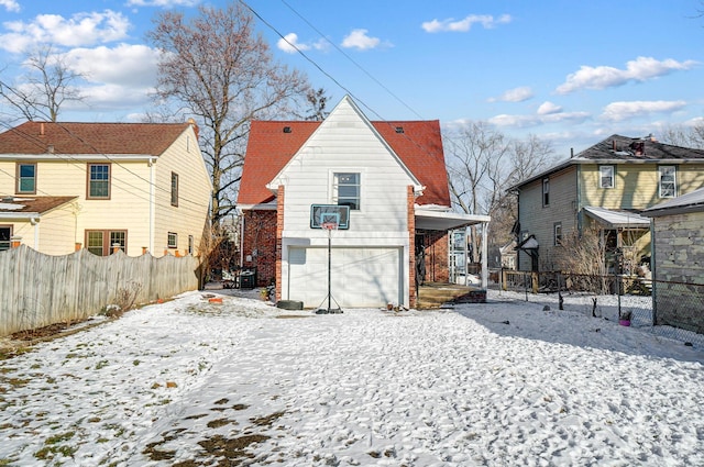 snow covered house featuring a garage, a residential view, fence, and brick siding