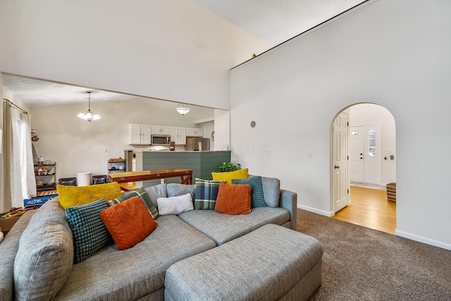 carpeted living room with a chandelier, arched walkways, a towering ceiling, and baseboards