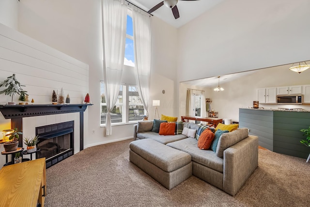 carpeted living room featuring a fireplace, a towering ceiling, a wealth of natural light, and a ceiling fan