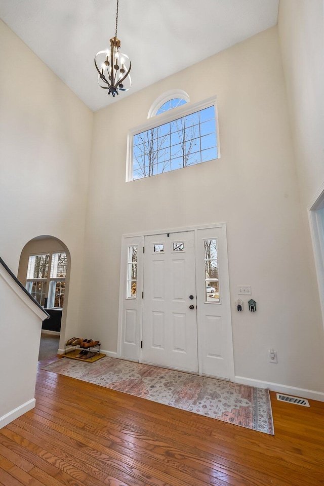 foyer featuring arched walkways, visible vents, a towering ceiling, baseboards, and hardwood / wood-style flooring