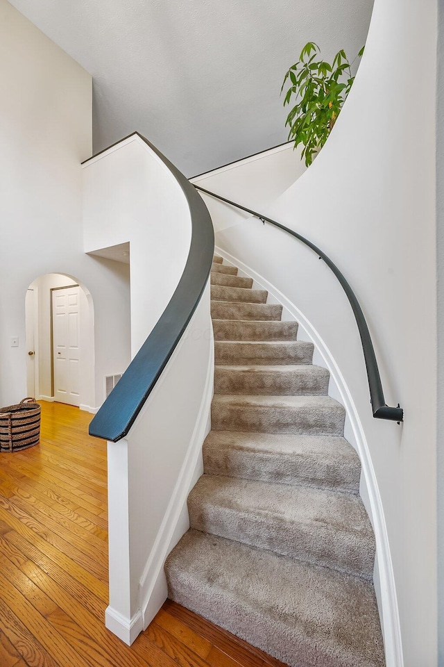 stairs with arched walkways, wood-type flooring, and baseboards