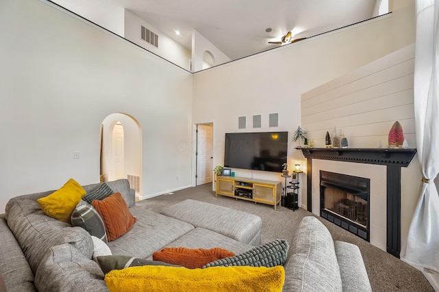 living area with visible vents, a tiled fireplace, arched walkways, and carpet flooring