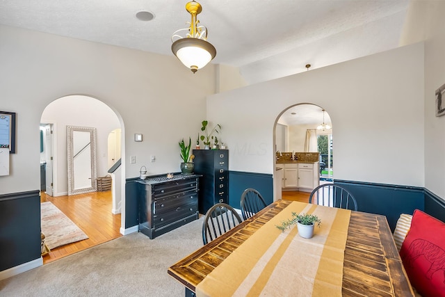 dining area featuring arched walkways, vaulted ceiling, light carpet, and baseboards