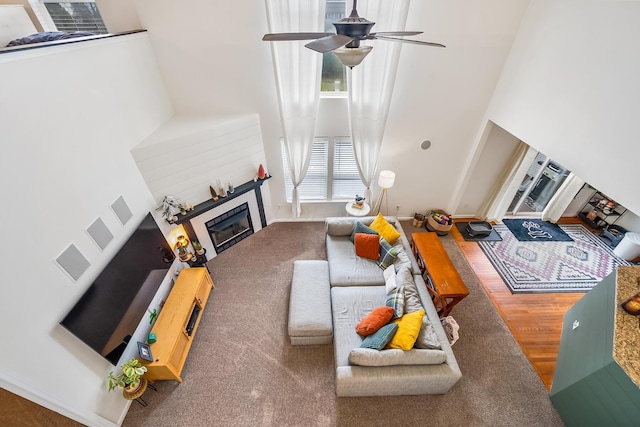 living room with visible vents, a ceiling fan, a tile fireplace, wood finished floors, and a high ceiling