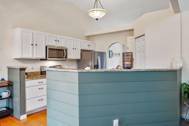 kitchen featuring white cabinets, light wood-style flooring, appliances with stainless steel finishes, light stone countertops, and vaulted ceiling