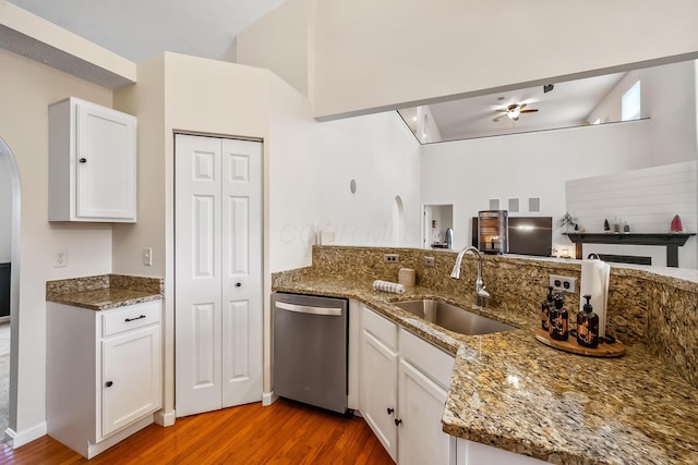 kitchen featuring wood finished floors, stainless steel dishwasher, stone counters, white cabinetry, and a sink