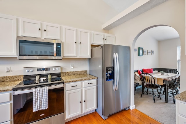 kitchen with arched walkways, white cabinets, light stone counters, appliances with stainless steel finishes, and light wood-style floors