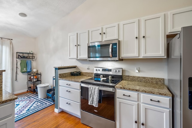 kitchen featuring light wood-style flooring, light stone counters, stainless steel appliances, a textured ceiling, and white cabinetry