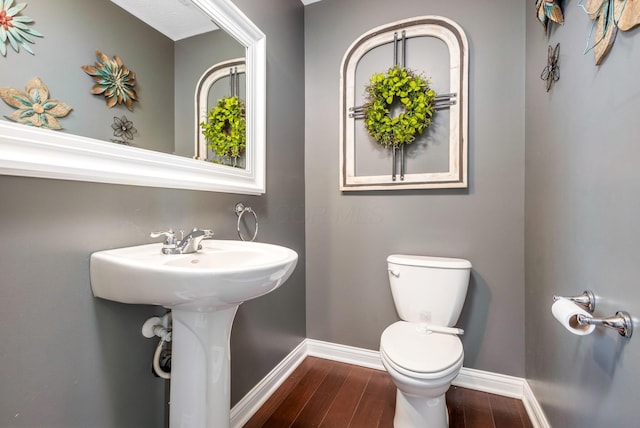 half bath featuring wood finished floors, toilet, and baseboards