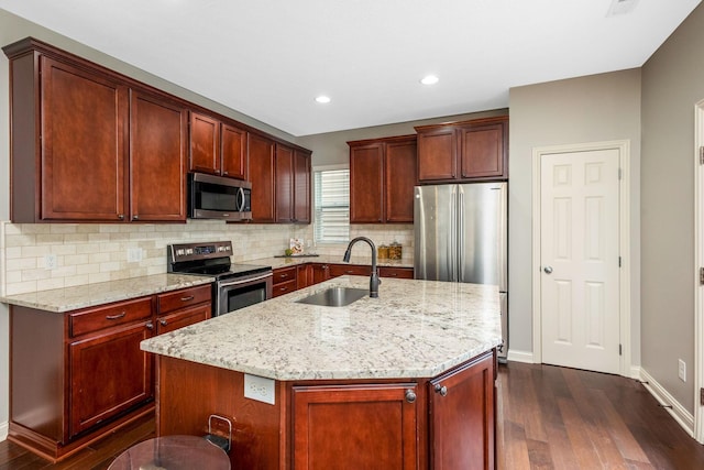 kitchen featuring appliances with stainless steel finishes, a center island with sink, light stone counters, and a sink