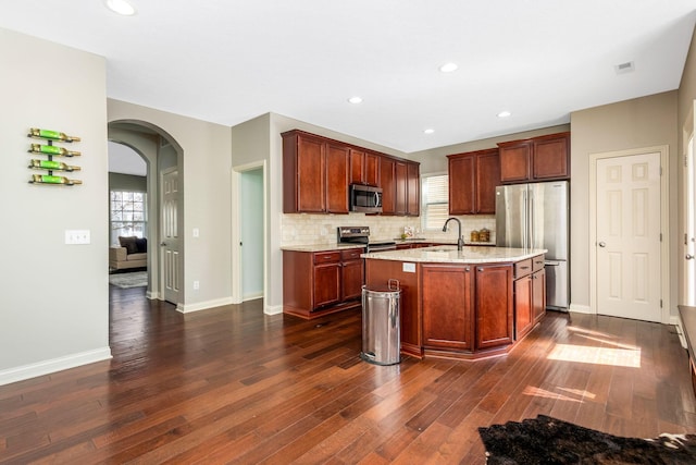 kitchen featuring arched walkways, a sink, a kitchen island with sink, stainless steel appliances, and a wealth of natural light