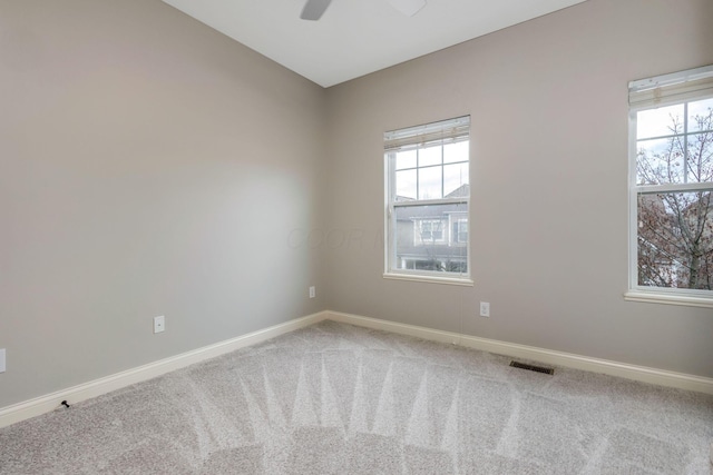 carpeted spare room featuring a ceiling fan, visible vents, and baseboards