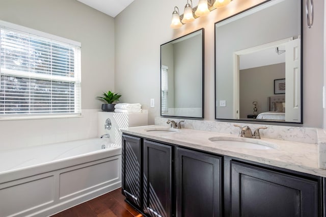 ensuite bathroom featuring a garden tub, wood finished floors, a sink, and ensuite bathroom